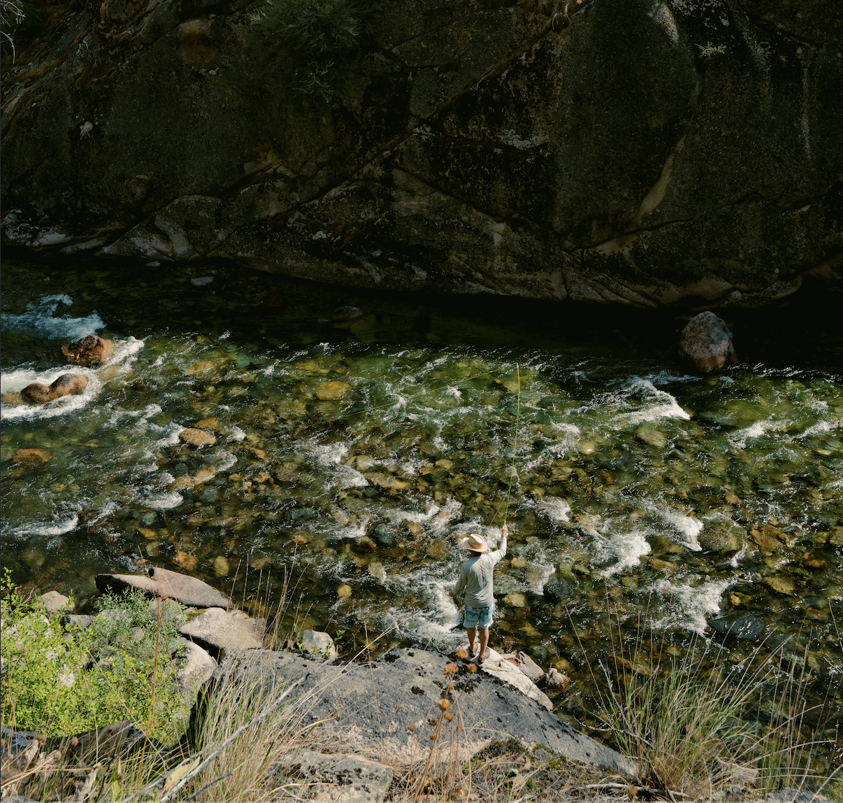 A view of a man fishing above a clear shallow river. 